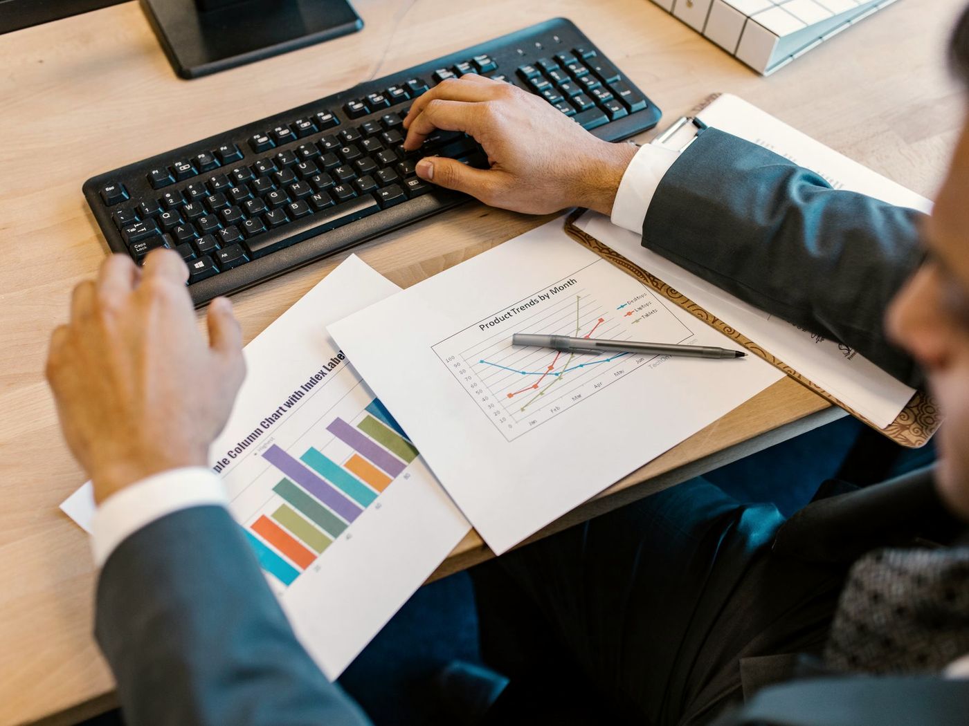 Hands on a keyboard beside printed sales charts