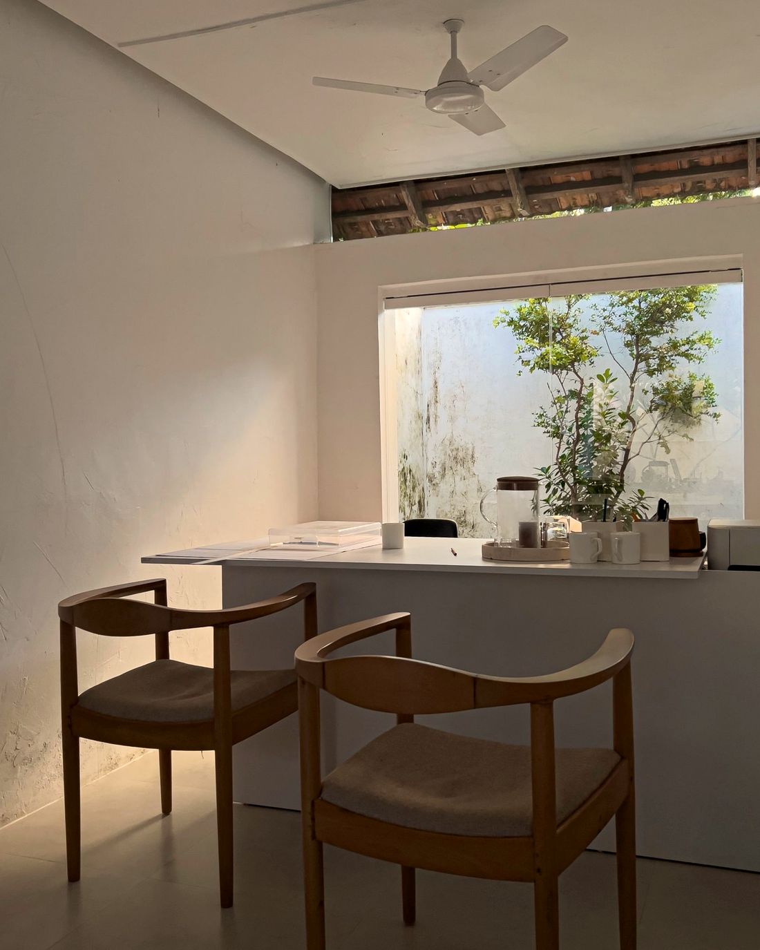 A calm, sunlit modern office with a desk and two wooden chairs